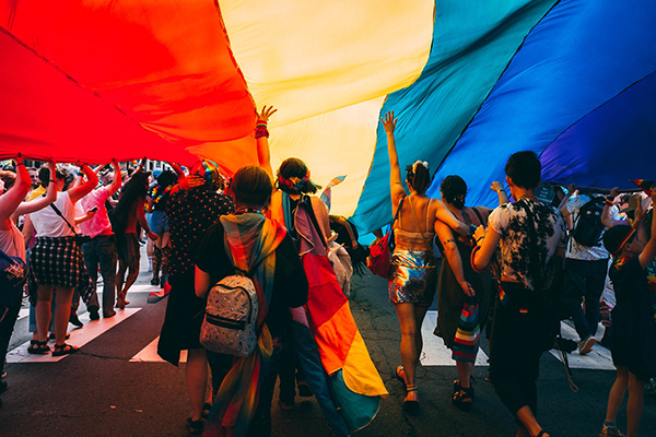 People under a rainbow flag. Photo by Mercedes Mehling