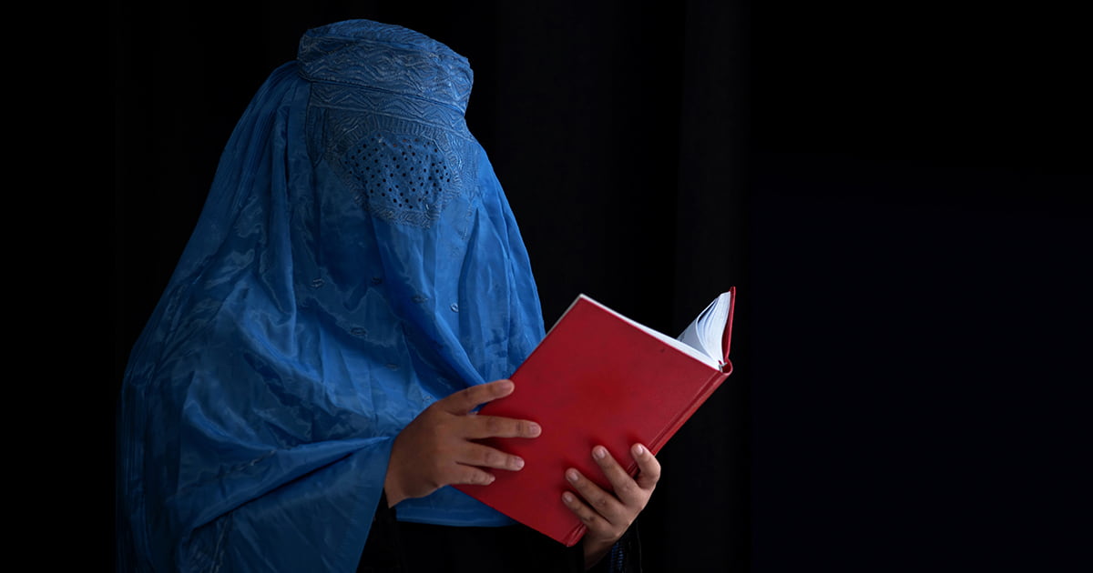 Veiled person reading a red book