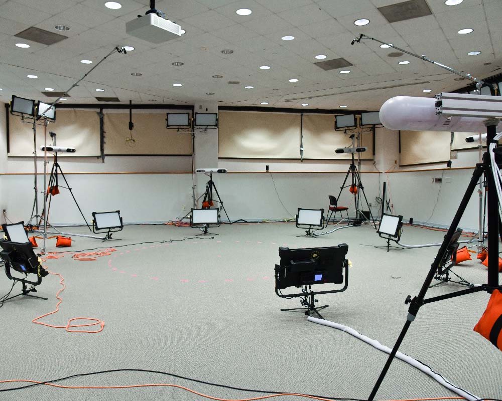 A large room with an empty center marked by an x, surrounded by lights and cameras for volumetric capture