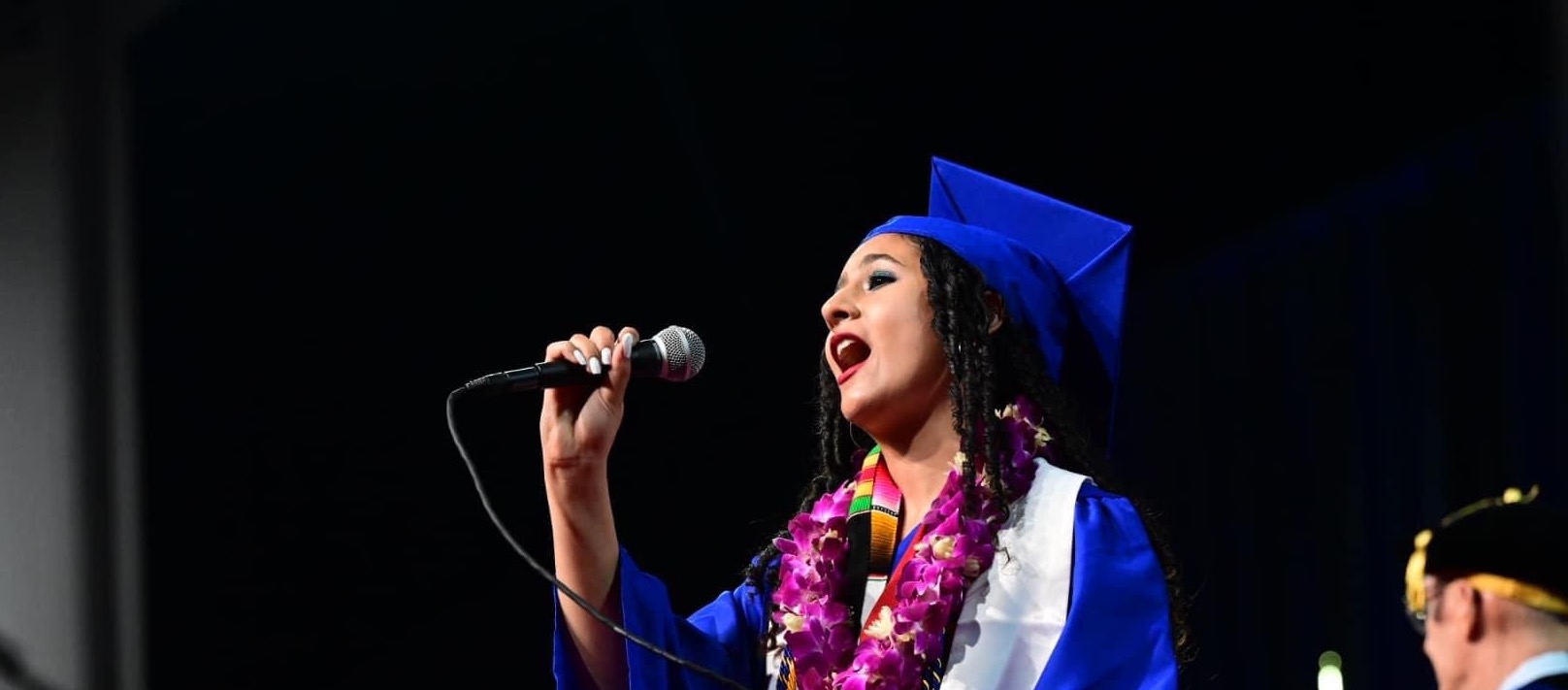Aisley Wallace Harper, dressed in graduation regalia, sings the national anthem at the CAS May 2023 graduation ceremony