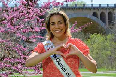 Jude Mabone, wearing a sash and tiara, makes a heart with her hands