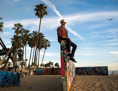 Matthias McCoy-Thompson wears a VR headset while sitting on a graffitied wall at Venice Beach