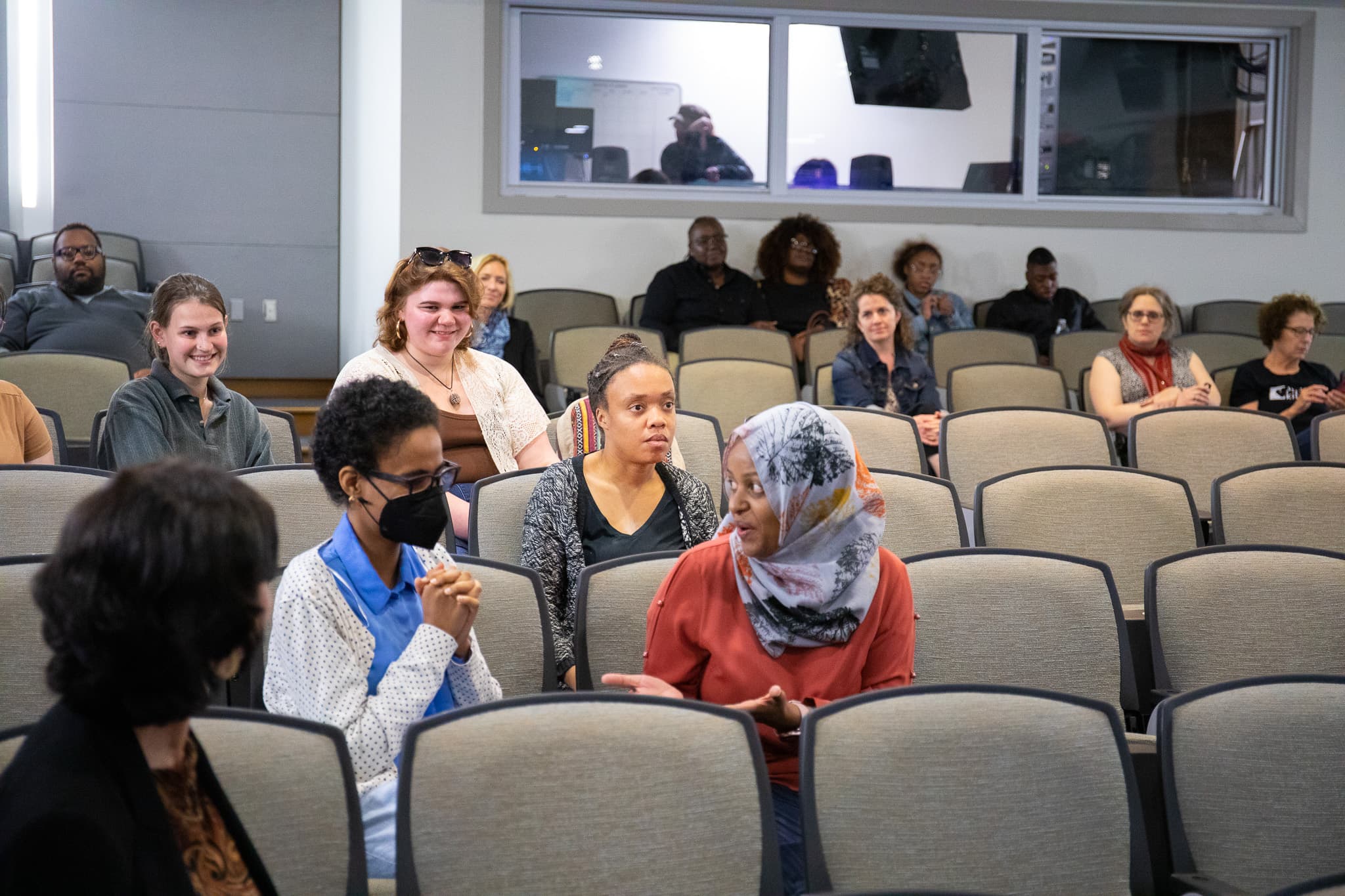 In the center of the image, one of the featured storytellers shares her experience participating in the documentary alongside a student. Members of the audience sit around them in an auditorium.