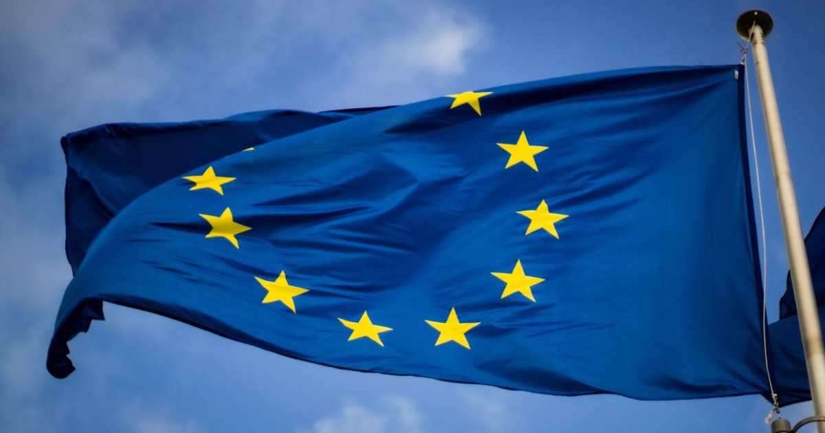 European Union flag on a flagpole blowing in the wind against blue sky.