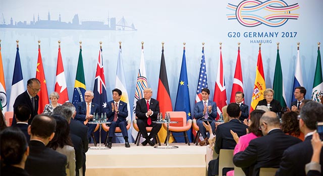world leaders sit on a stage with multiple country flags behind them at the 2017 G20 Summit