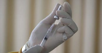 A hand holds a vaccine needle with a gloved hand