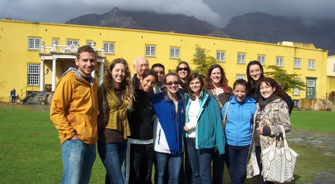 Students studying abroad standing in front of a yellow building and misty mountains.