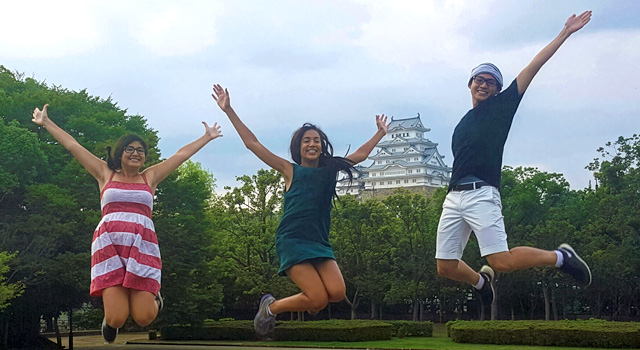 Smiling students jump for a photo in front of a historic building in Japan.