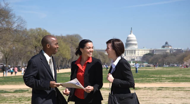 A diverse group of three people stand talking on the Washington Mall in front of the U.S. Capitol