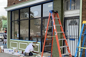 A storefront with a ladder in front of it and a man painting its exterior wall
