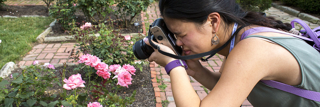 A discover the world of communication student photographs roses outside with a film camera