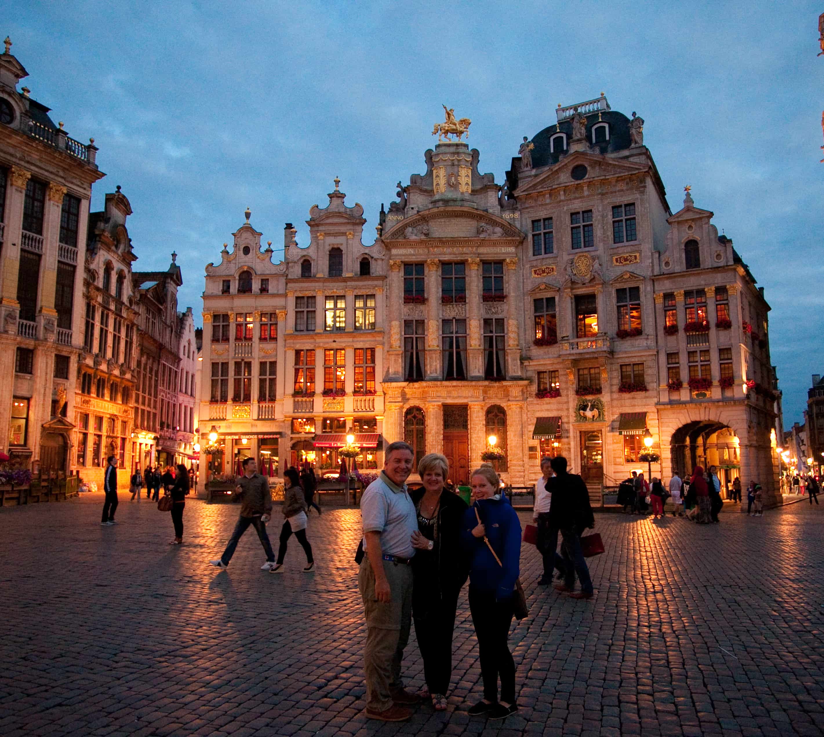 Three people stand together in a plaza during an evening in Brussels