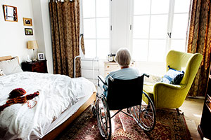 Elderly woman in wheelchair facing window.