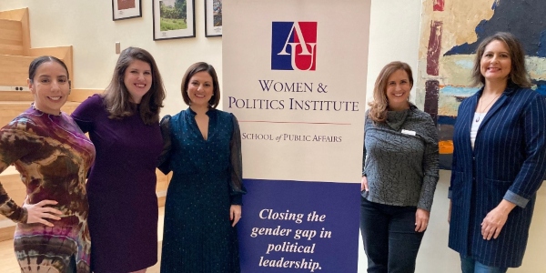 five professional women of mixed race standing next to an American University banner