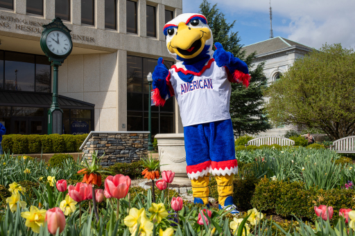 Mascot Clawed stands in front of the library's garden, with a bed of tulips in front of him.