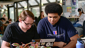 Students work on a laptop covered in AU stickers