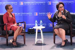 Two women sitting in chairs in front of American University backdrop.