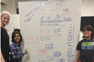 Math professor Jaime Miller with two students in front of a white board with math problems.